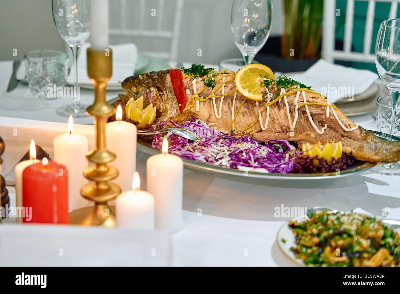 Ein wunderschön präsentiertes Gericht mit ganzen Fisch garniert mit Kräutern, Zitrone und farbenfrohem Gemüse, elegant für ein besonderes kulinarisches Erlebnis. Stockfoto