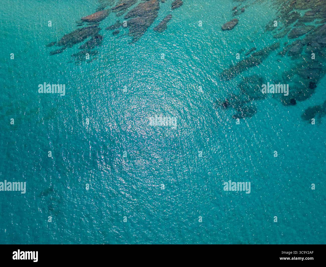 Blick aus der Vogelperspektive auf das türkisfarbene Meer mit Unterwasserfelsen, die durch klares Wasser sichtbar sind. Ruhige Oberfläche reflektiert Sonnenlicht an einem ruhigen Sommertag Stockfoto
