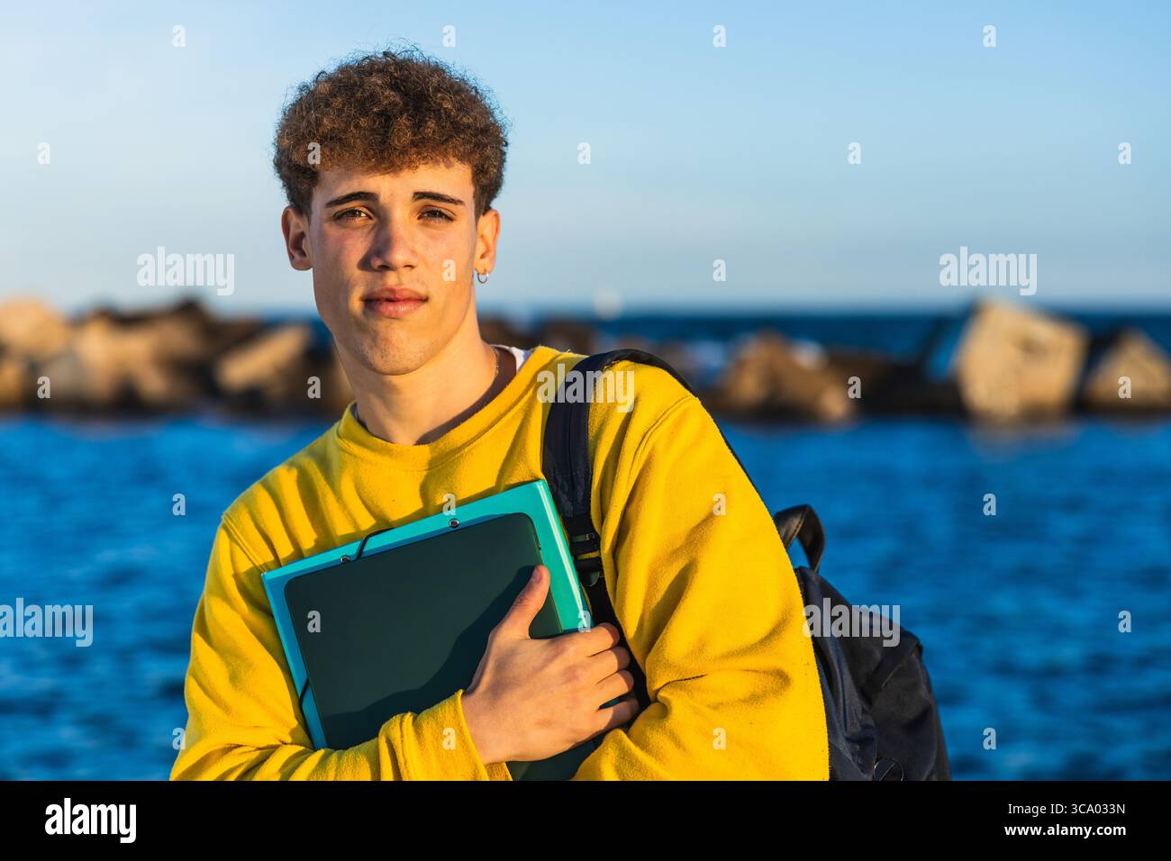 Junge Studentin, die Bücher am Meer bei Sonnenuntergang hält Stockfoto