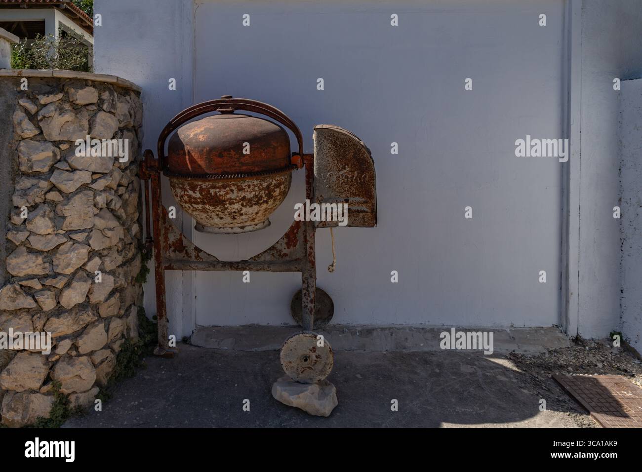 Ein alter, rostiger Betonmischer sitzt vor dem Garagentor. Stockfoto