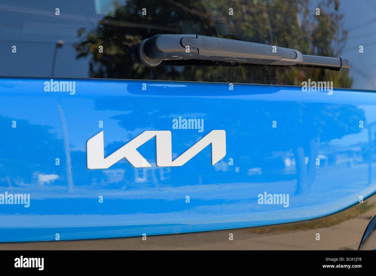 Rückansicht eines blauen Kia-Fahrzeugs mit dem aktualisierten silbernen Emblem der Marke und einem schwarzen Heckscheibenwischer über dem Logo. Stockfoto