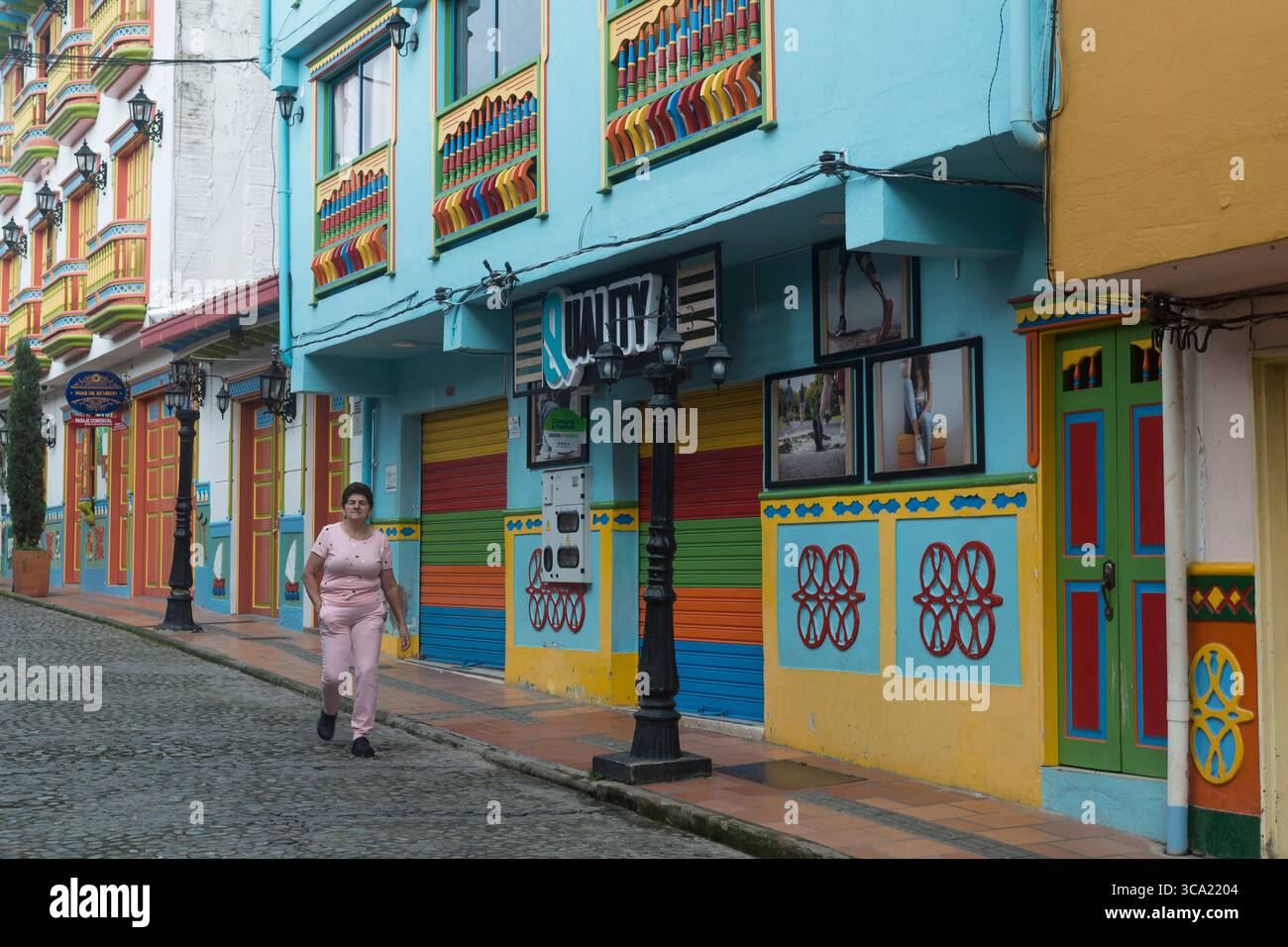 Frau in rosa Kleidung, die in einer Straße mit bunten Häusern in Guatapé, Antioquia Department, Kolumbien läuft Stockfoto