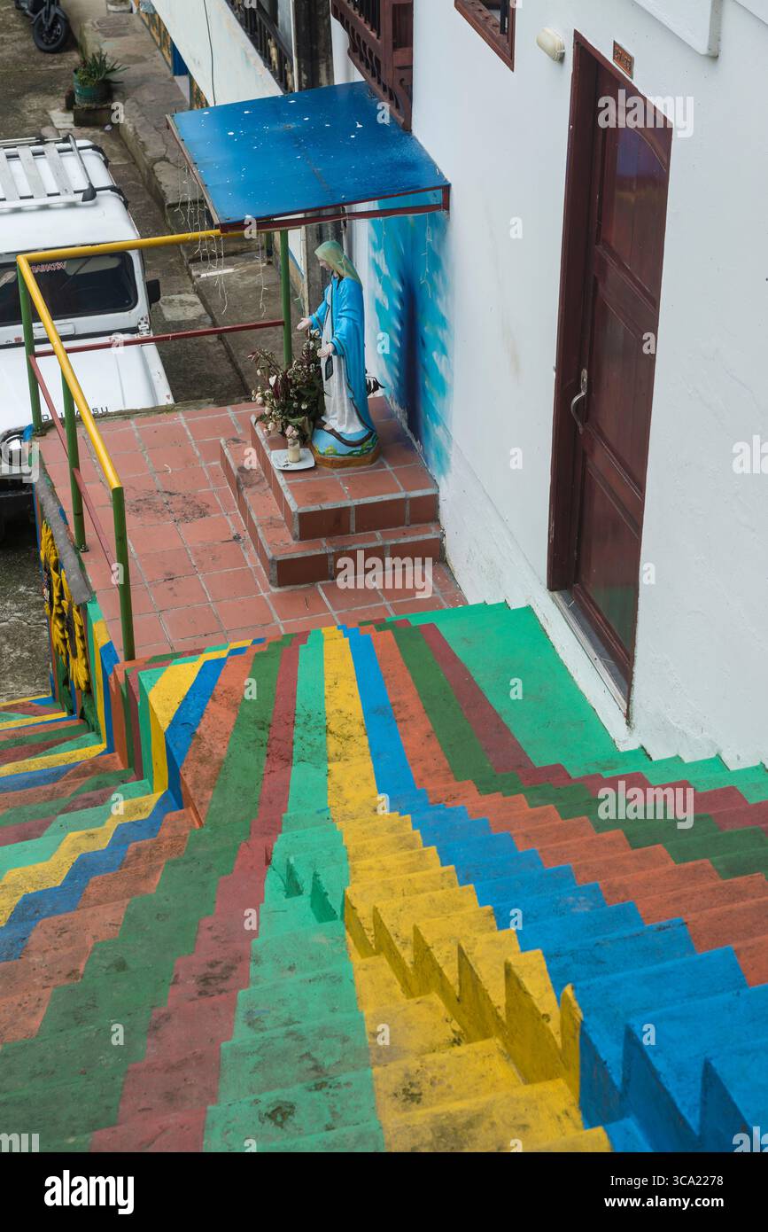 Mehrfarbige Linien auf Treppen, die an einer Marienstatue unter einem Baldachin in einem Haus in Guatapé, Antioquia Department, Kolumbien, zusammenkommen Stockfoto