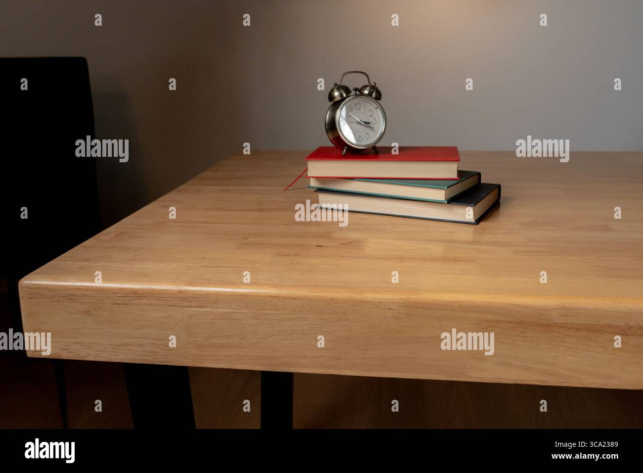 Klassischer Wecker auf Büchern mit warmer Beleuchtung in ruhiger Innenumgebung. Stockfoto