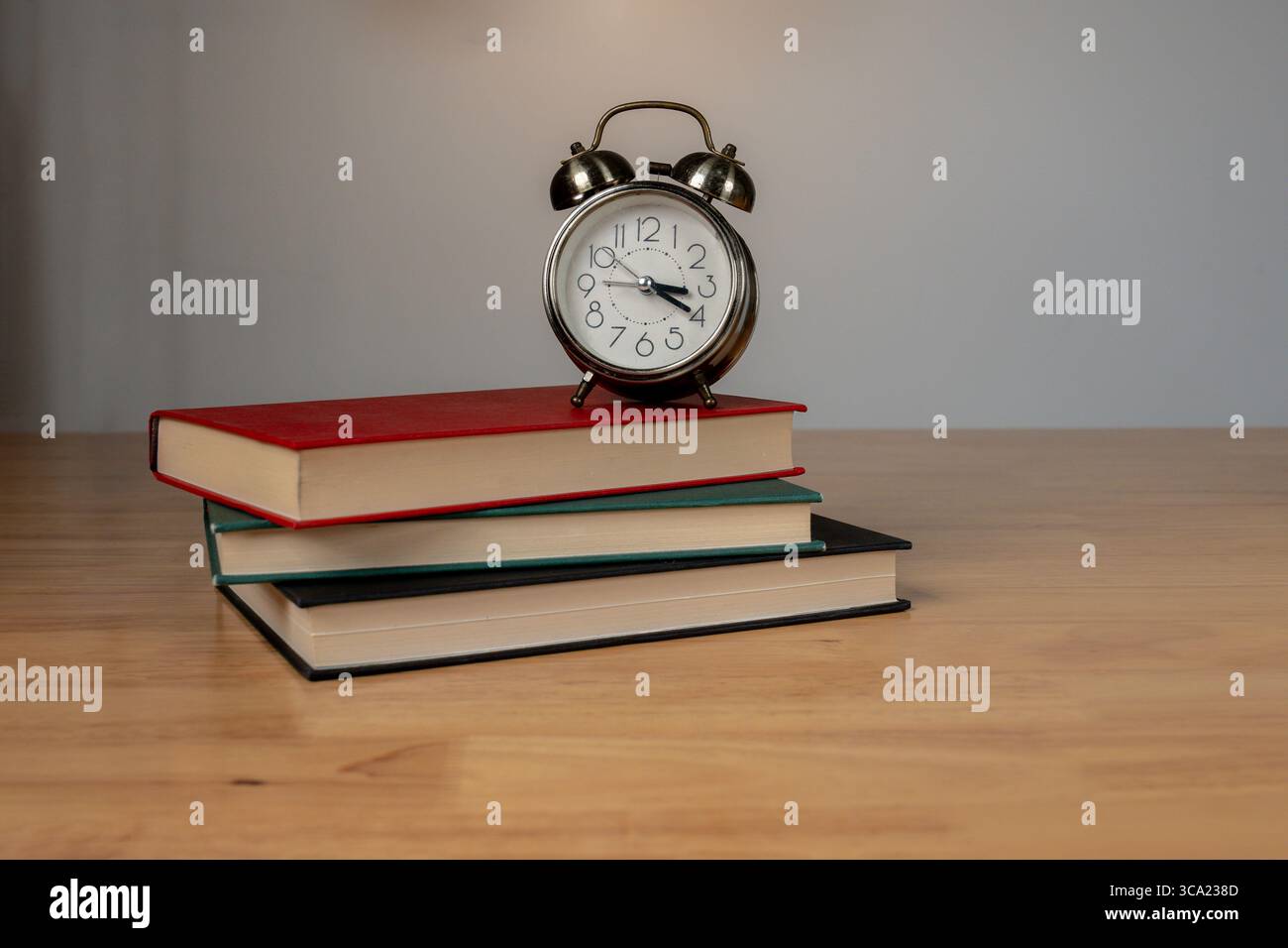 Klassischer Wecker auf Büchern mit warmer Beleuchtung in ruhiger Innenumgebung. Stockfoto