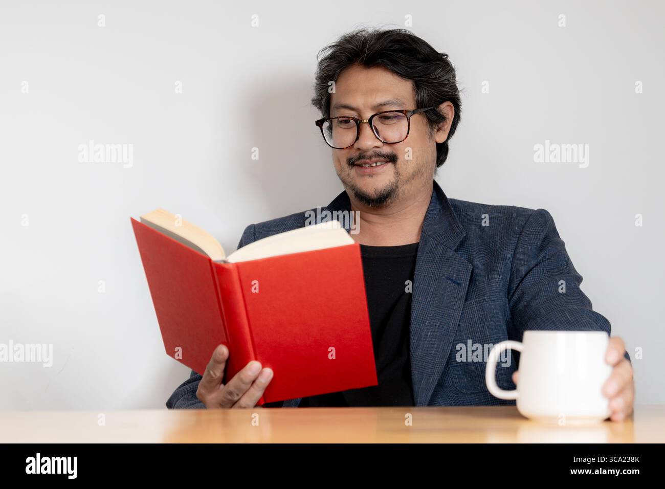 Entspannter junger Mann mit Brille, der in gemütlicher Atmosphäre ein Buch liest. Stockfoto