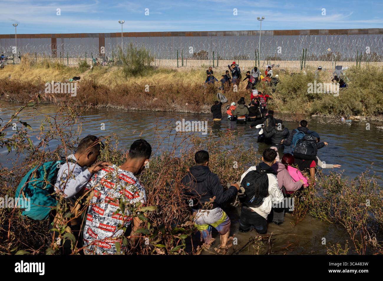 Zivilisten, darunter Kinder, navigieren durch einen Fluss am hoch aufragenden Grenzzaun in der Nähe von Ciudad Juarez, um in die USA zu gelangen Stockfoto