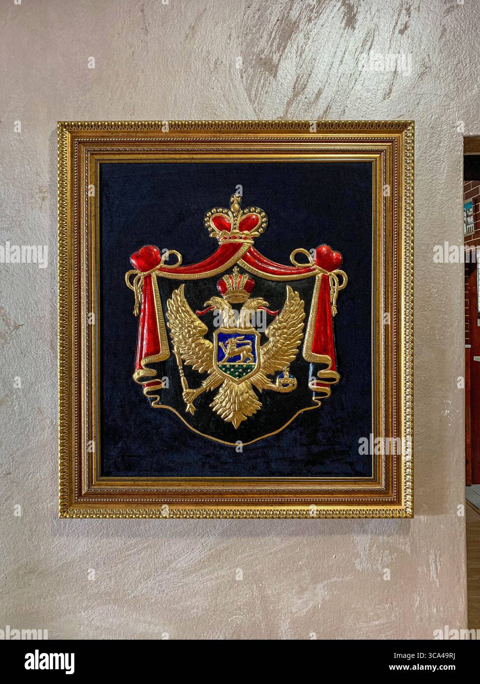 Cetinje, Montenegro. August 2025. Eine gerahmte Schnitzerei des Wappens Montenegros vor der republik, mit einer monarchischen Version des nationalen Wappens mit einem doppelköpfigen Adler und gekröntem Mantel, an der Wand eines ausländisch touristisch orientierten Restaurants mit konservativen, nationalistischen und patriotischen Dekorationselementen. Diese Version des Wappens wurde während der Zeit des Fürstentums und Königreichs (19.–Anfang des 20. Jahrhunderts) verwendet, bevor 2004 das moderne Staatssymbol auf der Nationalflagge eingeführt wurde. Quelle: Kevin Izorce/Alamy Live News Stockfoto