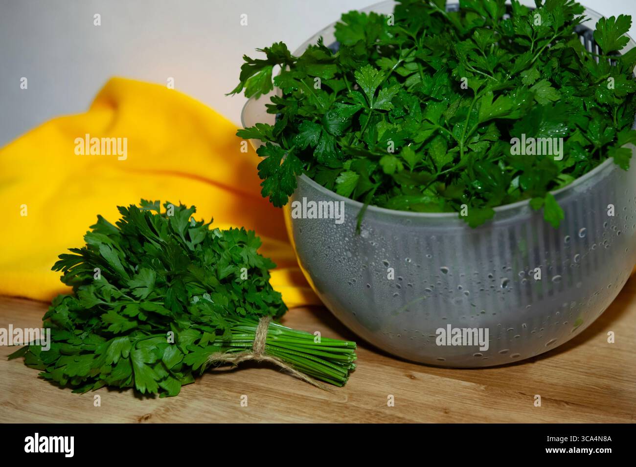 Petersilie mit Gemüse in Salatschleuder - bunte Küchenvorbereitung mit gelbem Tuch. Stockfoto