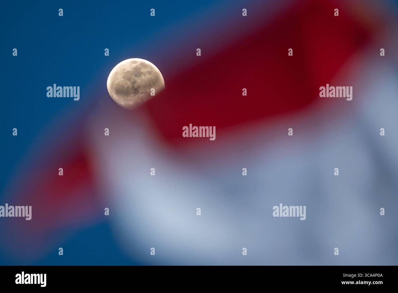 Ein Mond, der am Abendhimmel leuchtet, mit der winkenden Flagge der Republik Indonesien im Vordergrund, der als Monat der Unabhängigkeit markiert Stockfoto