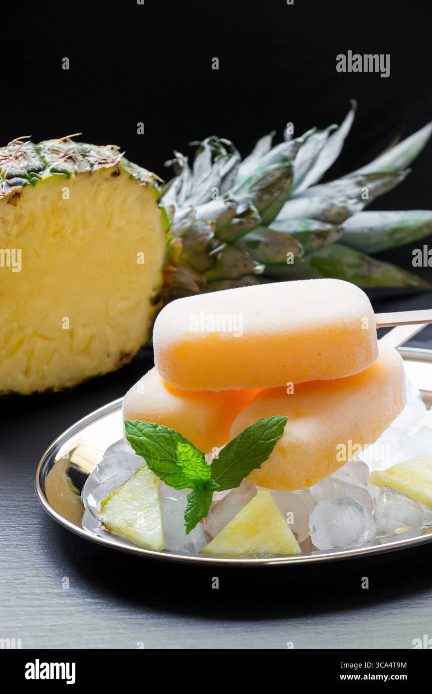 Ananassorbet-Eis-Eis-Eis auf Silberplatte mit Eiswürfeln gehackte Ananasscheiben, Minze nahe in halbe Ananas auf schwarzem Hintergrund geschnitten. Ananassorbet-Eis-Eis. Vertikal. Stockfoto