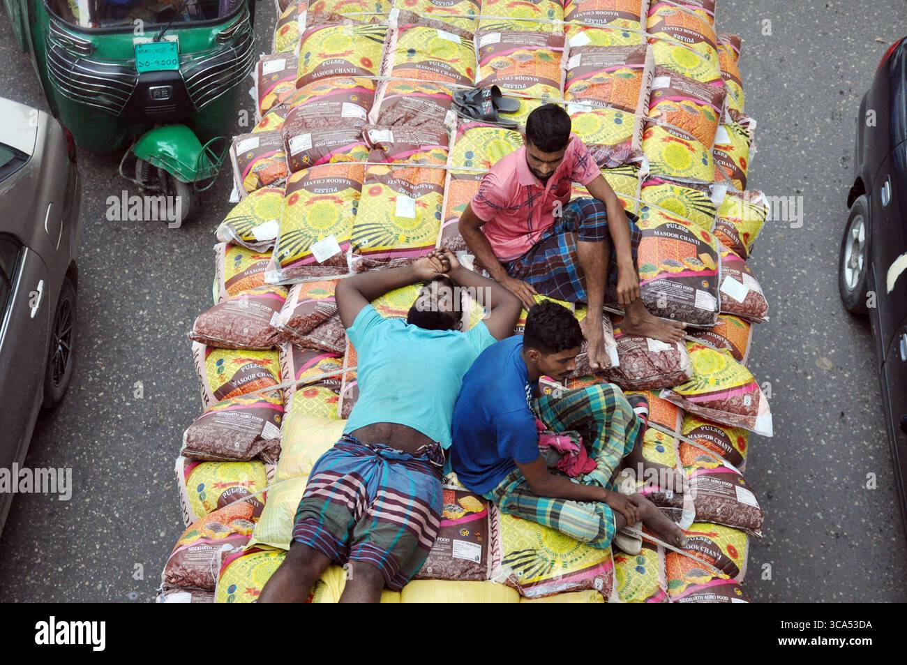 Dhaka, Segunbagicha, Bangladesch. August 2025. 6 Agust, Dhaka Bangladesch: In Dhakas belebten Straßen nimmt die Sicherheit oft einen Rückstand auf die Notwendigkeit. Mit Gütern beladene Kleintransporter sind zu einem unkonventionellen Transportmittel für verzweifelte Pendler geworden. Ohne Platz im Inneren klettern die Menschen auf gestapelte Fracht und liegen flach, um Polizei- oder Stromleitungen zu vermeiden. Jede Kurve, jede plötzliche Bremse birgt die Gefahr, zu einem tödlichen Ende zu fallen Für viele ist es kein Abenteuer, sondern eine harte Realität, die von Armut und mangelndem Transport getrieben wird. Die Behörden warnen vor der Praxis, aber in einer Stadt erstickt mit t Stockfoto