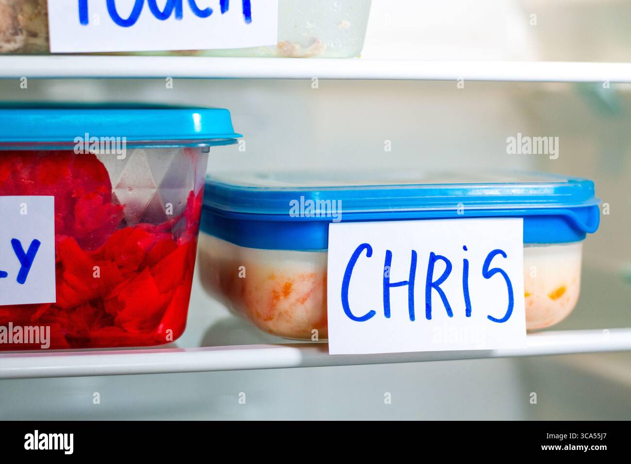 Bürocontainer mit handgeschriebenen Namensschildern in einem gemeinsamen Kühlschrank. Gesunde Lebensmittelvorbereitung für das Arbeitsbüro-Studium. Stockfoto