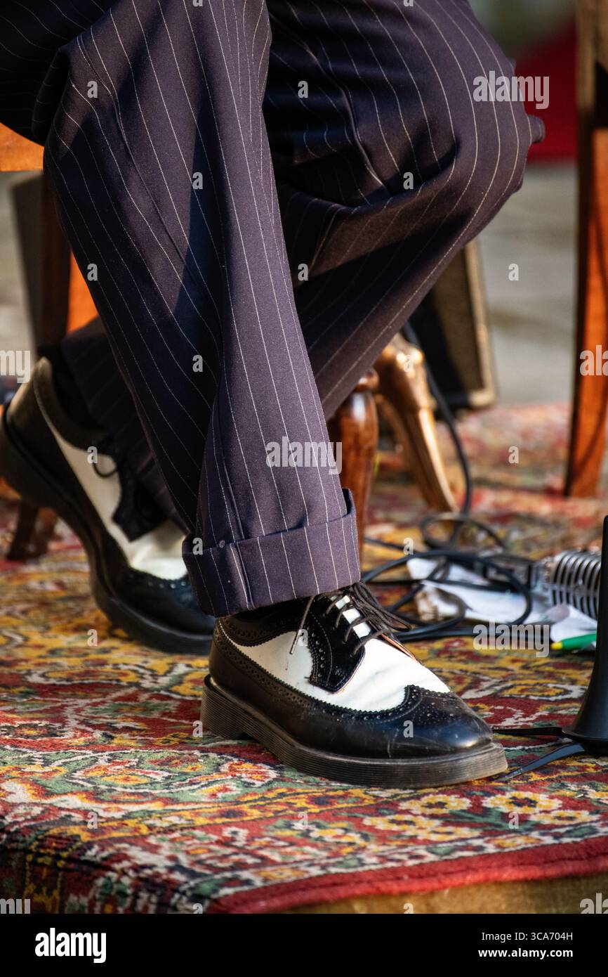 Nahaufnahme der klassischen zweifarbigen Schuhe eines Jazzmusikers mit Nadelstreifenhose auf einem gemusterten Teppich. Stockfoto