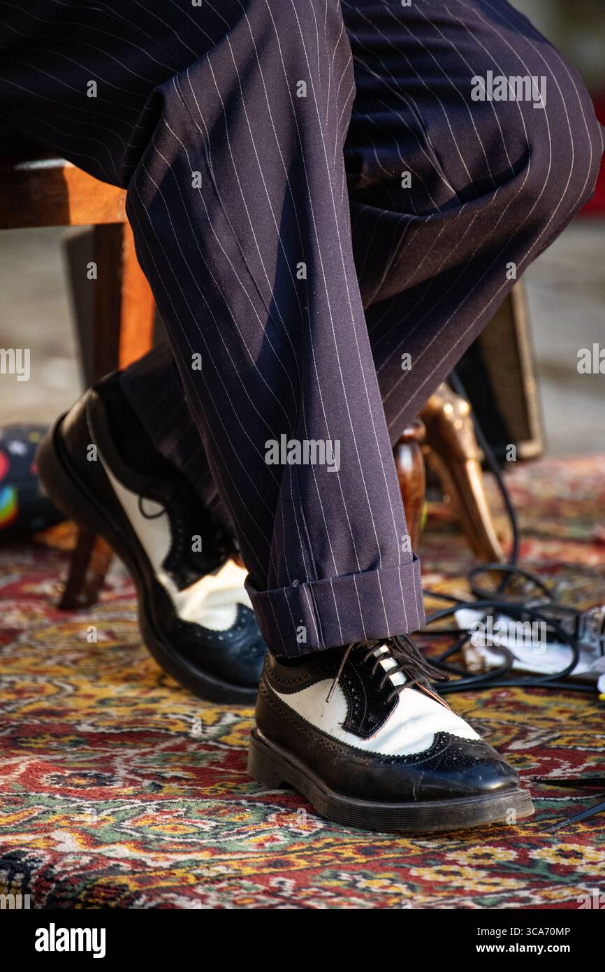 Nahaufnahme der klassischen zweifarbigen Schuhe eines Jazzmusikers mit Nadelstreifenhose auf einem gemusterten Teppich. Stockfoto