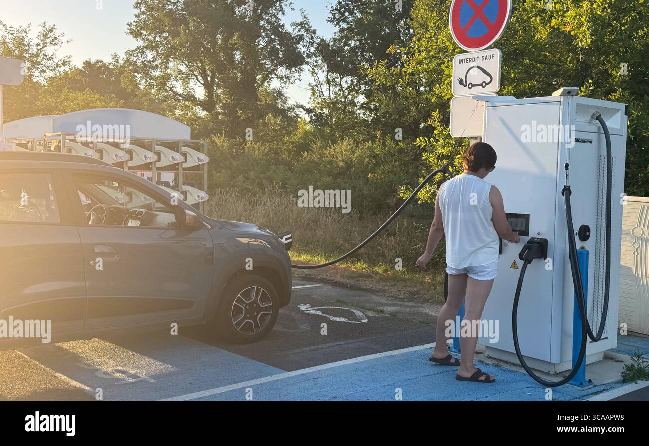 Die Frau schaltet die Autoladestation ein, während sie ihr Elektrofahrzeug auflädt. Konzept intelligenter Technologien für komfortables Wohnen, Elektrofahrzeuge Stockfoto