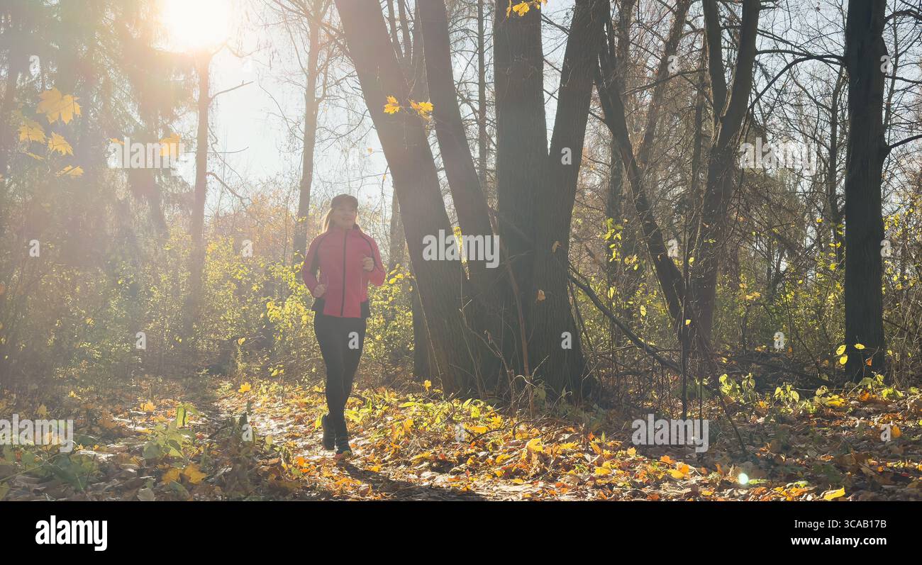 Waldweg im Herbst. Herbstläuferin, die in wunderschönen Laubwäldern läuft, Natur Hintergrund. Asiatische glückliche Sportfrau, die im Freien trainiert. Stockfoto