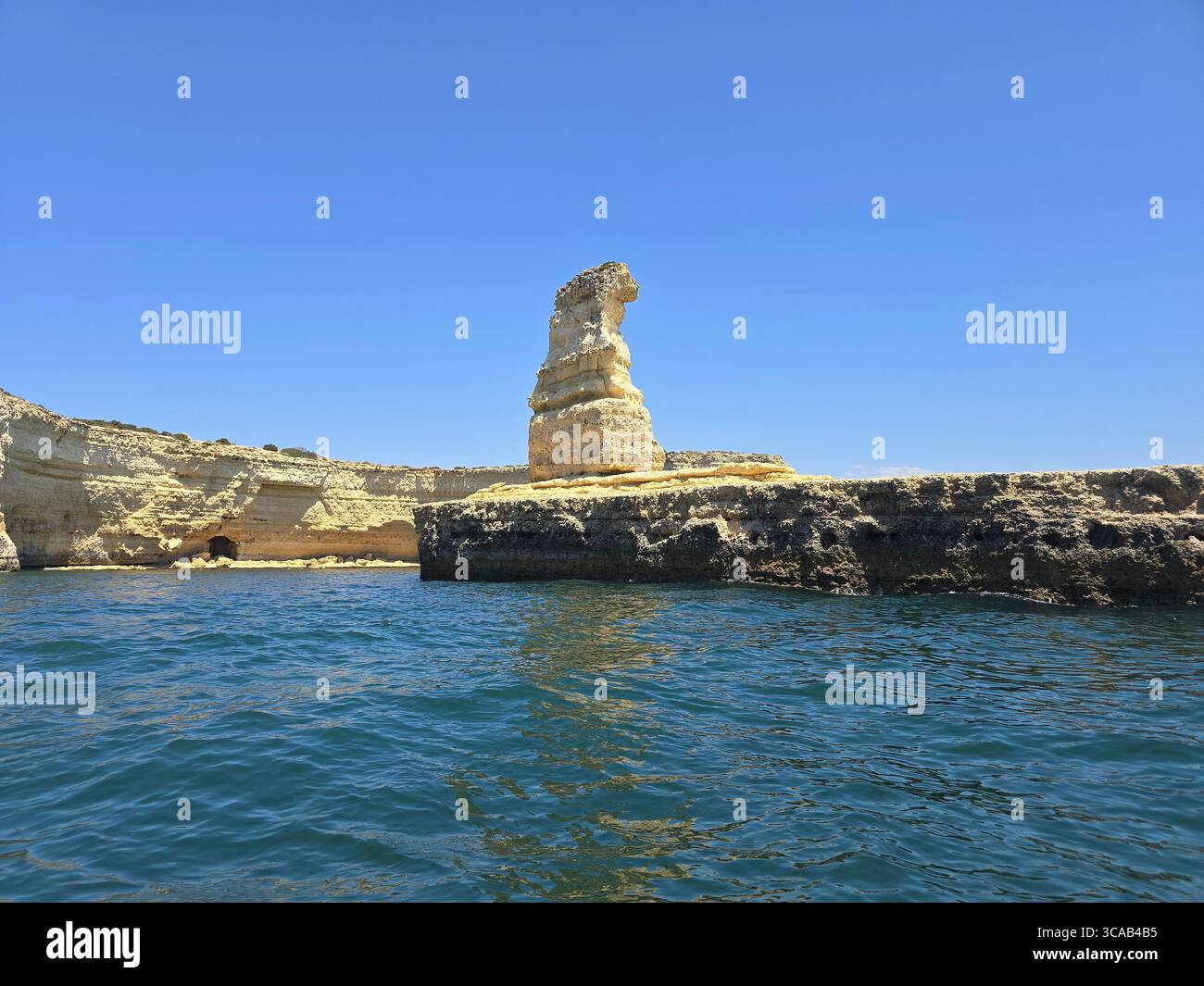 Markanter Meeresstapel, der von der Küste entlang der Algarve im Süden Portugals aufsteigt, umgeben von ruhigen Gewässern des Atlantiks unter einem klaren blauen Himmel. - Smartphone-aufgenommenes Stockfoto