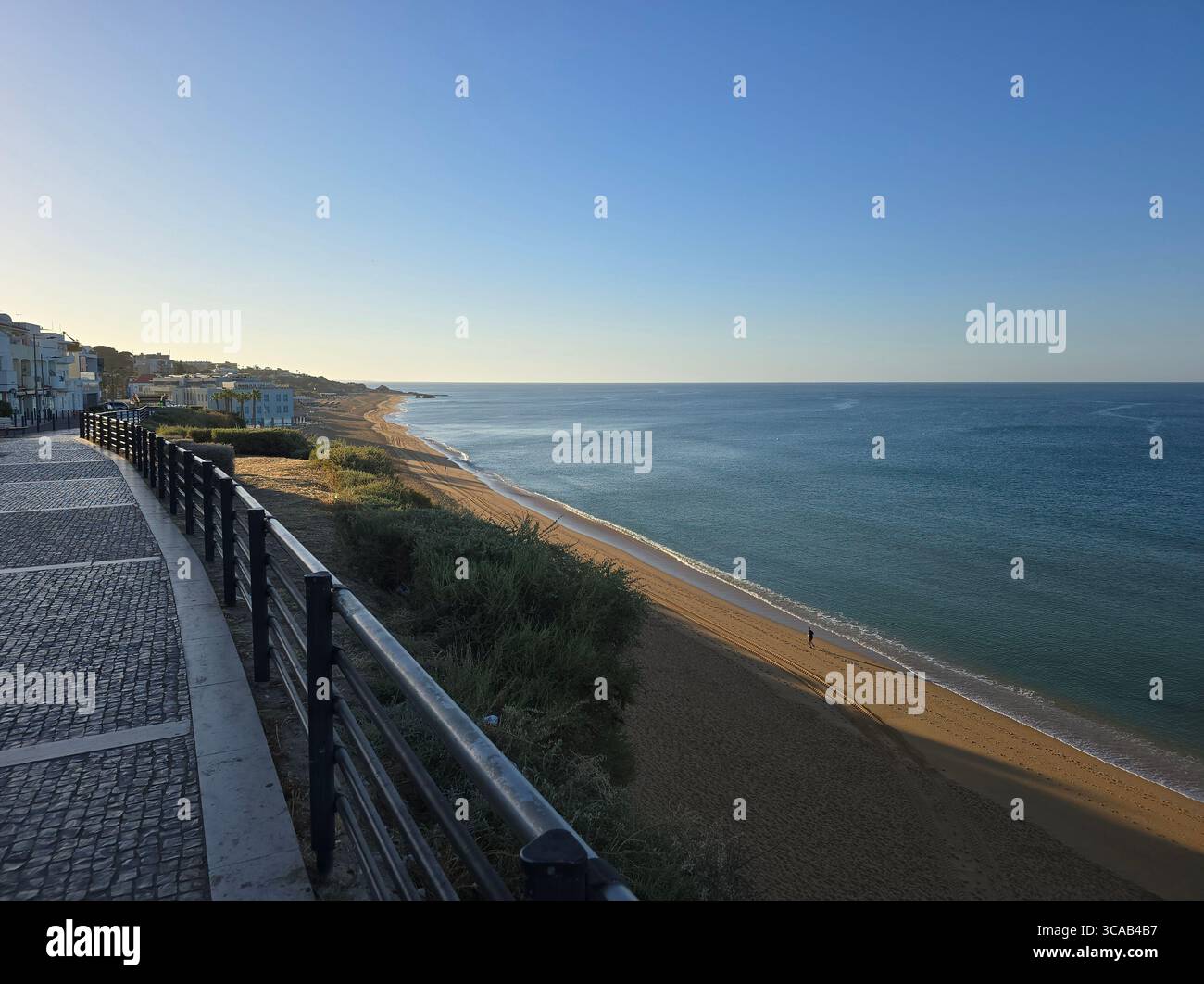 Ruhiger Blick auf den Strand und die Promenade von Albufeira bei Sonnenaufgang in der Algarve, Portugal, mit dem ruhigen Atlantik und der leeren Küste. - Smartphone-aufgenommenes Stockfoto