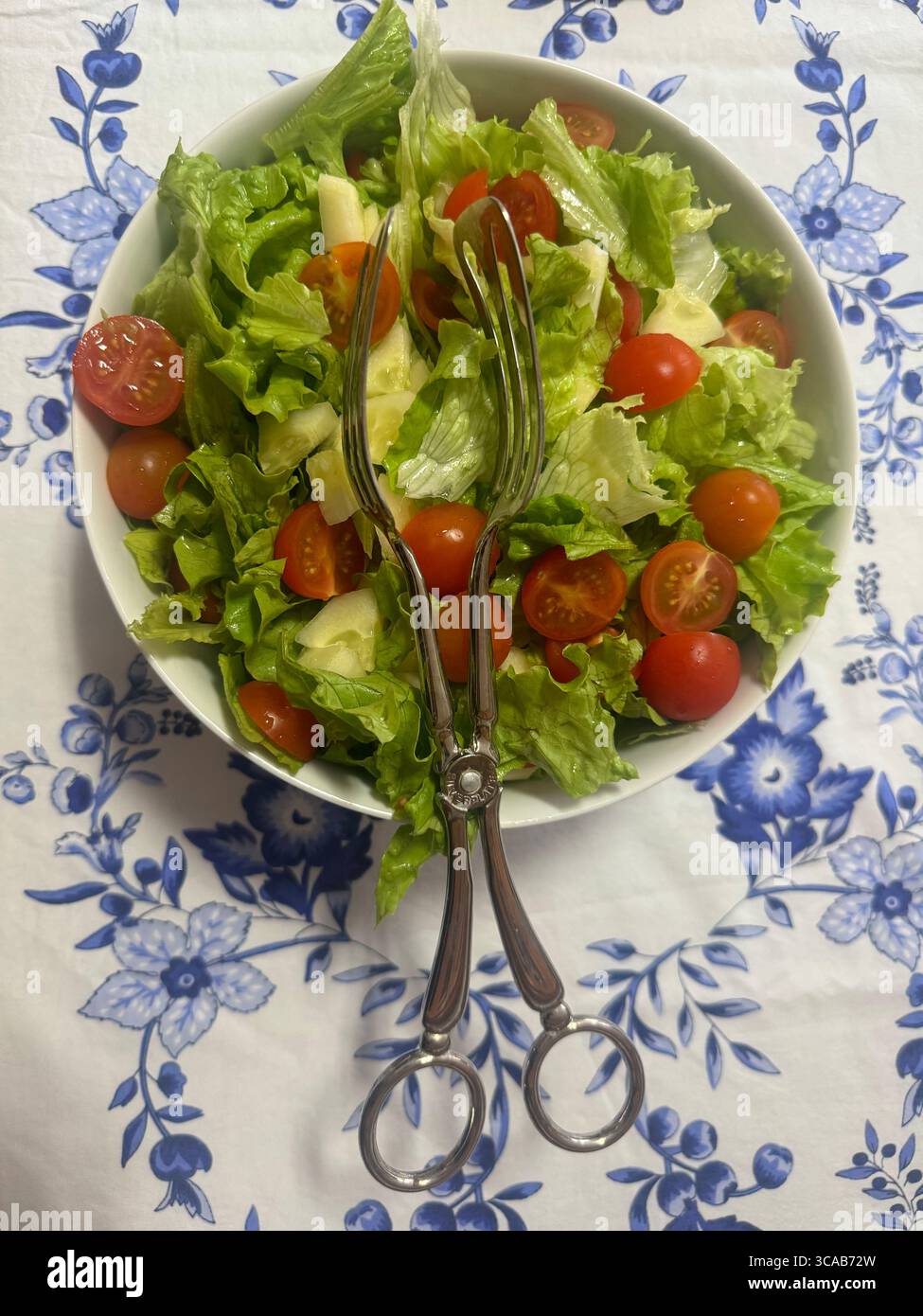 Frischer Gartensalat in einer weißen Schüssel mit einer alten Salatzange auf einer blau-weiß gemusterten Tischdecke. - Smartphone-aufgenommenes Stockfoto