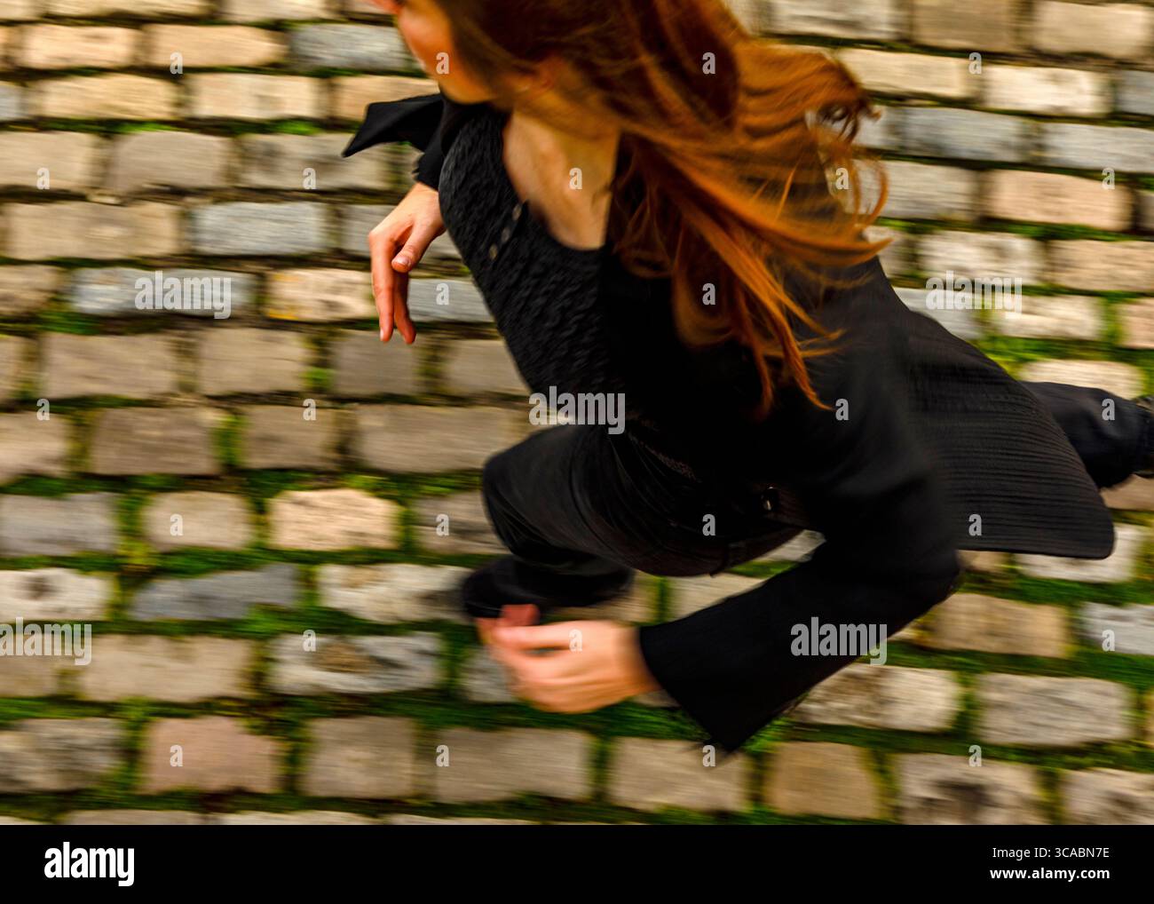 Eine Frau mit langen roten Haaren läuft auf einem Kopfsteinpflasterweg. Stockfoto