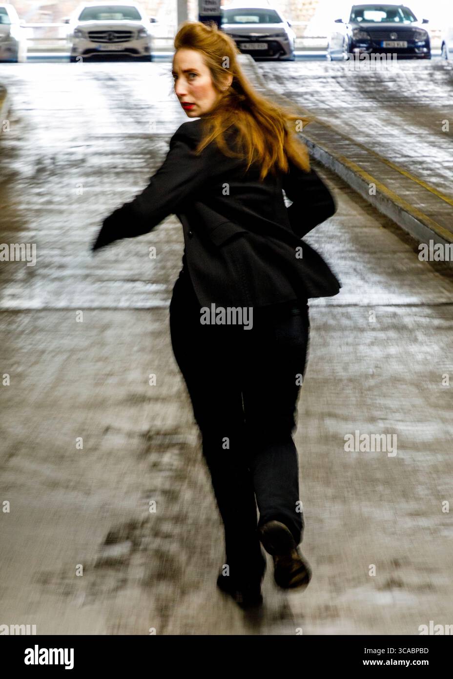 Eine Frau in einem schwarzen Anzug rennt vor der Kamera in einem Parkhaus weg. Stockfoto