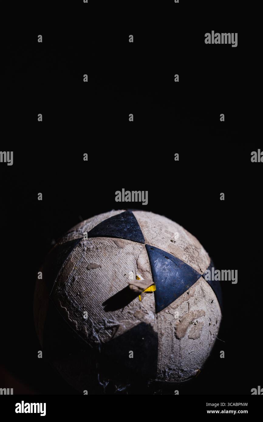 Beschädigter gelber, schwarzer und weißer Fußball vor schwarzem Hintergrund Stockfoto