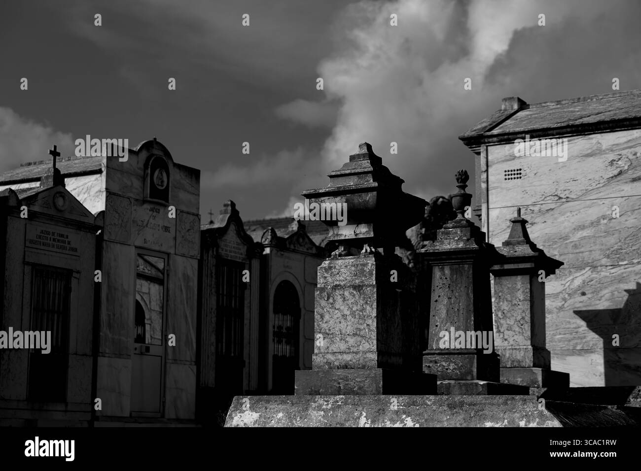 Auf dem 1839 gegründeten Almada-Friedhof in Lissabon stehen Steinmausoleen und kunstvoll verzierte Urnen vor einem dramatischen Himmel, der Erbe und feierliche Schönheit einfängt. Stockfoto