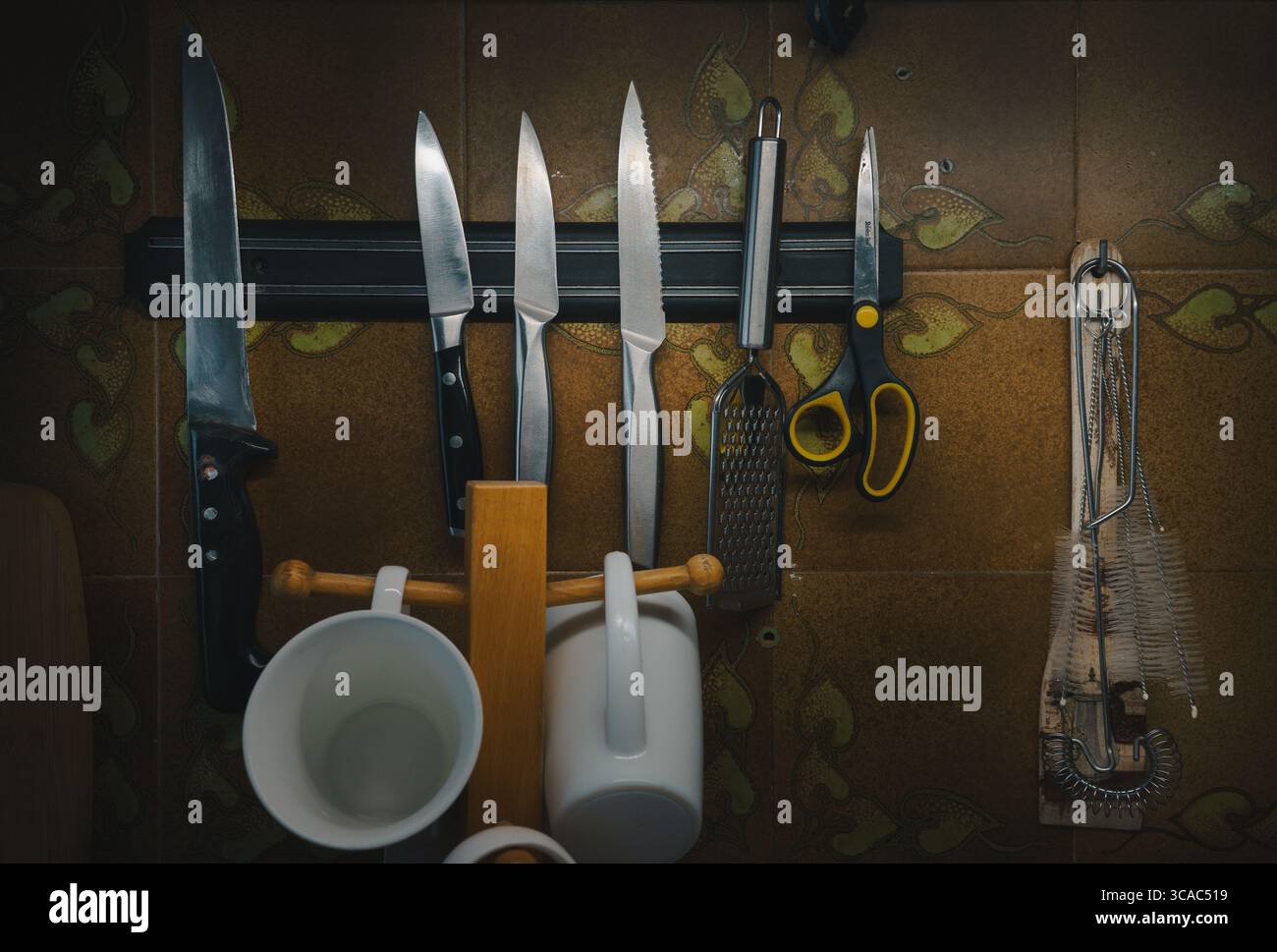Küchenmesser und anderes Zubehör auf einem Magnetstreifen an der Wand mit dekorativen Fliesen. Stockfoto