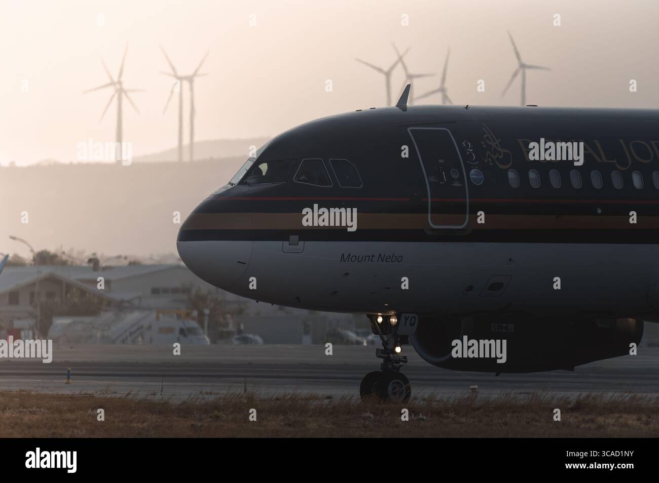 Larnaca, Zypern - 29. Juni 2024: Das jordanische Flugzeug fährt bei Sonnenuntergang auf der Landebahn, Windräder und Flughafengebäude im Hintergrund Stockfoto