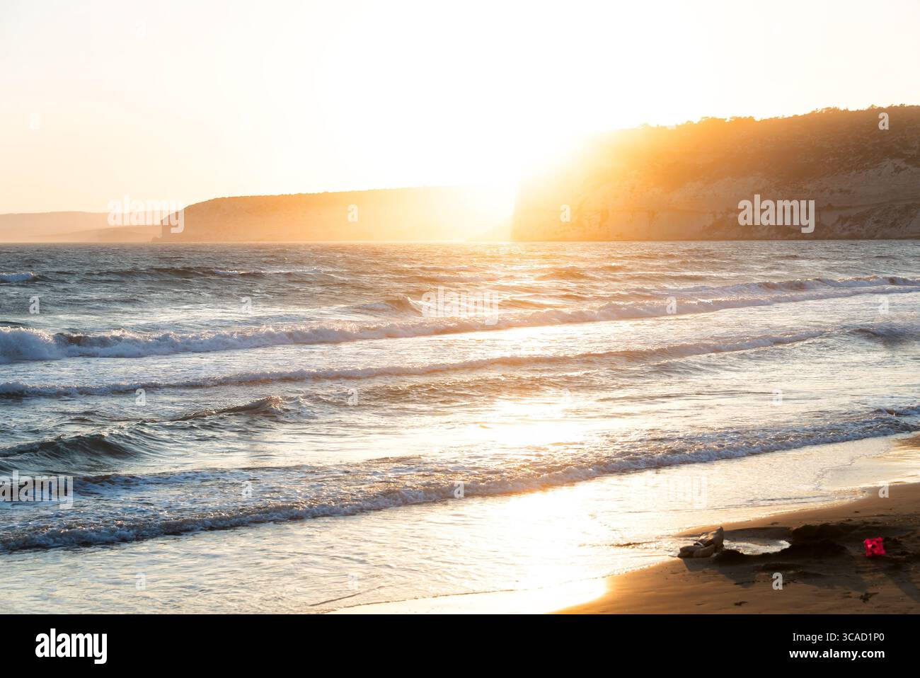 Sanfte Wellen am Ufer des Kourion Strandes bei Sonnenuntergang schaffen eine warme und einladende Atmosphäre Stockfoto