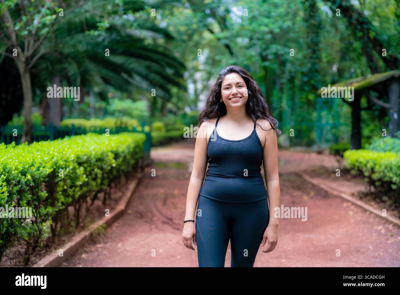 Sportliche junge Lateinfrau, die auf einem roten Kiesweg inmitten von Bäumen im Parque México läuft, einem berühmten grünen Platz in Condesa, ideal zum Joggen von Rela Stockfoto