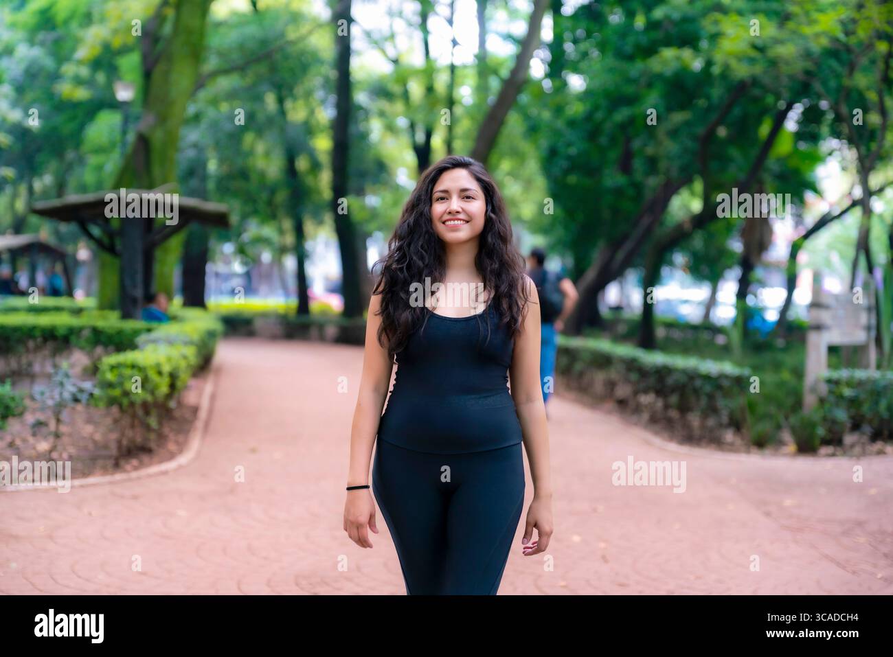 Sportliche junge Lateinfrau, die auf einem roten Kiesweg inmitten von Bäumen im Parque México läuft, einem berühmten grünen Platz in Condesa, ideal zum Joggen von Rela Stockfoto