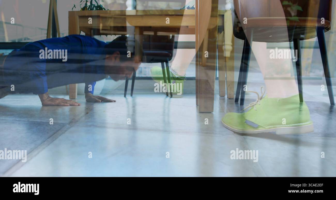 Mann in blauem Hemd, der Liegestütze auf Fliesenboden unter dem Tisch macht, mit grünen Schuhen, Kopierraum Stockfoto