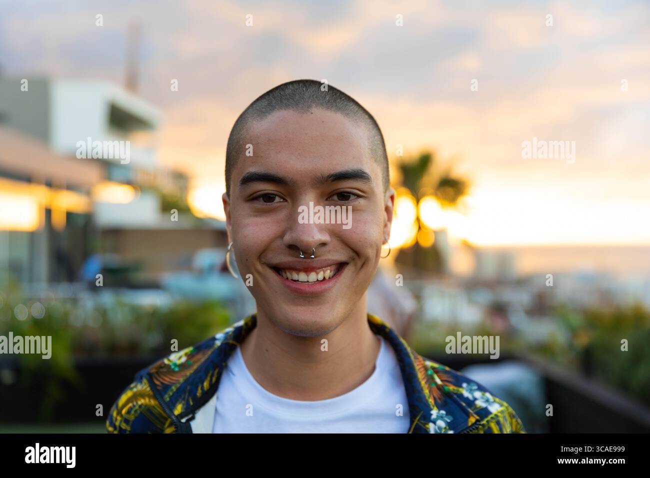 Asiatischer Mann, der bei Sonnenuntergang auf der Dachterrasse stand, trug ein Hemd mit Septumring und Creolen-Ohrring Stockfoto