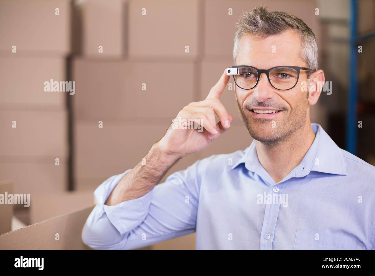 Mann mittleren Alters, der auf eine intelligente Brille zeigt, während er Pappkartons im Lager, Kopierraum packt Stockfoto