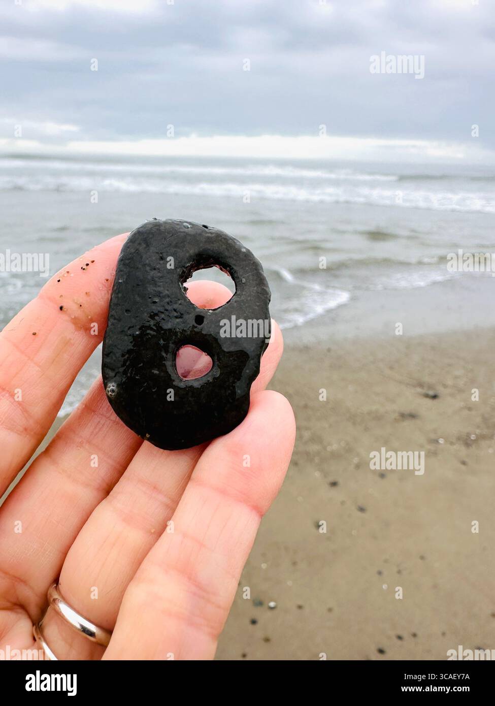 Nahaufnahme einer Hand, die einen Stein hält, an einem Strand in Lincoln City, Oregon. - Smartphone-aufgenommenes Stockfoto