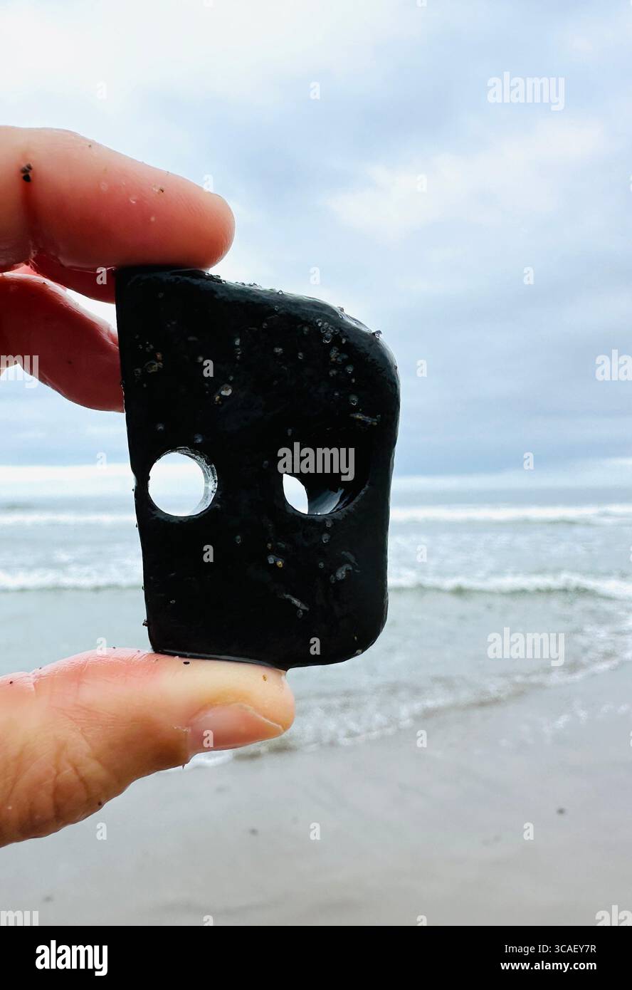 Nahaufnahme einer Hand, die einen Stein hält, an einem Strand in Lincoln City, Oregon. - Smartphone-aufgenommenes Stockfoto