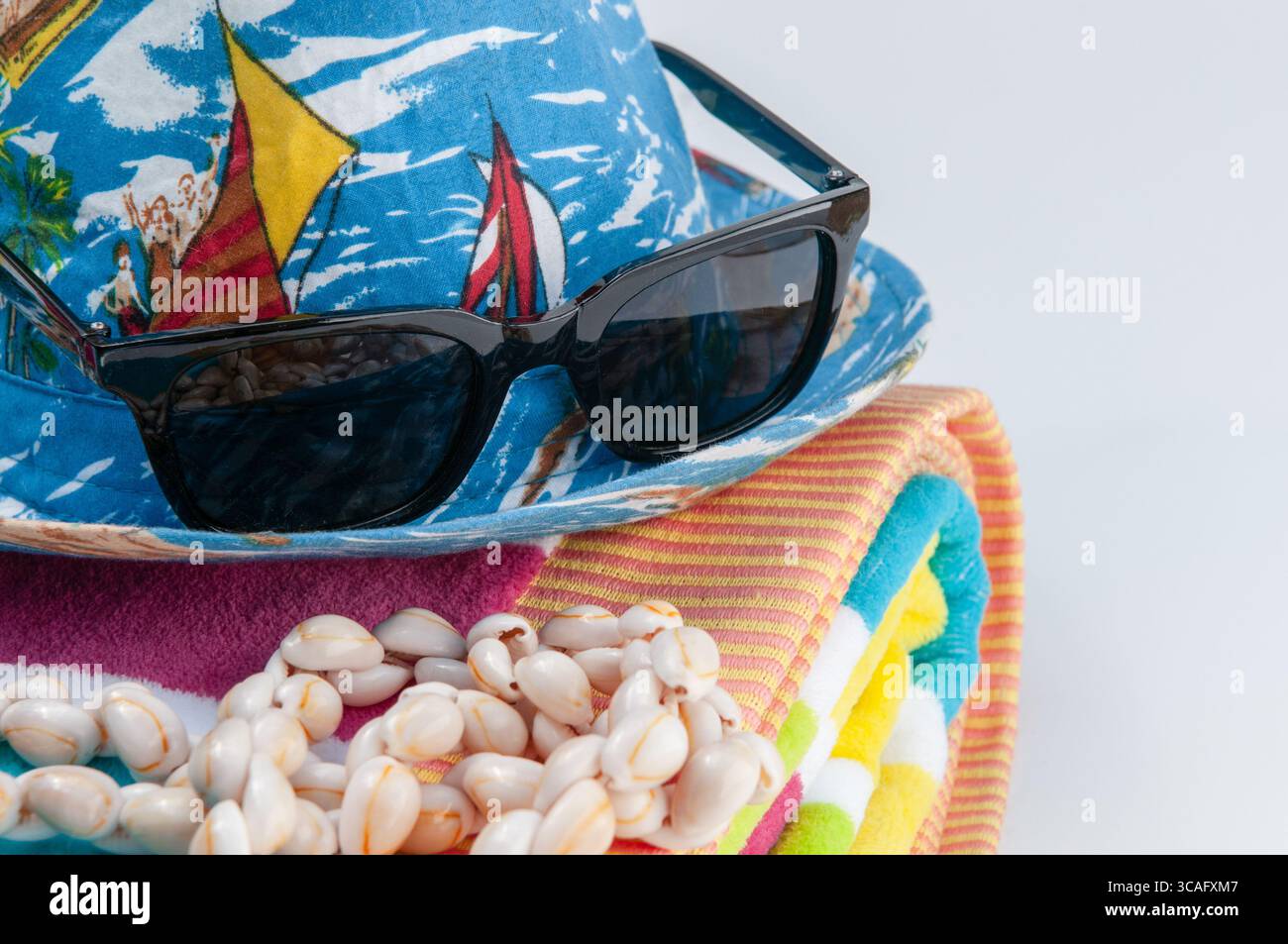 Ein blauer Baumwollfedora mit schwarzer Sonnenbrille und ein neongestreiftes Strandtuch mit einer Halskette mit Kaurimuscheln. Stockfoto
