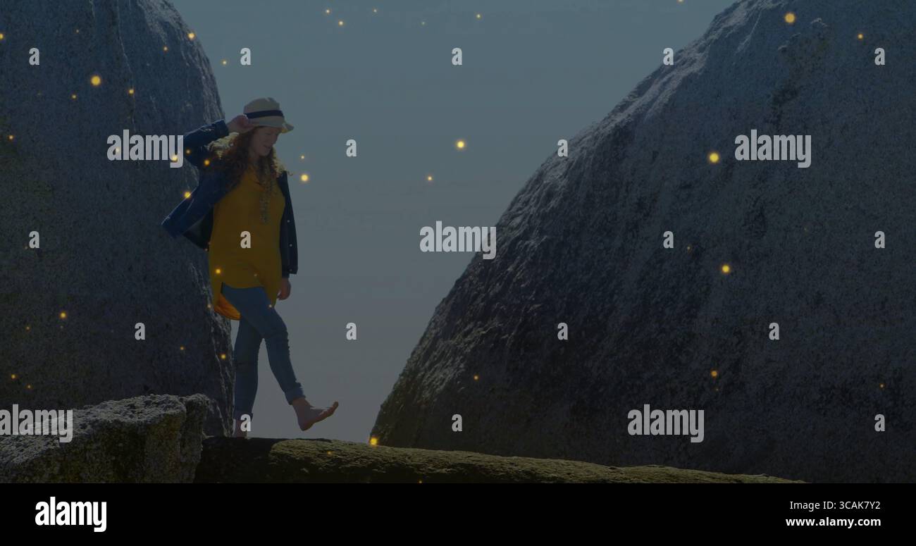 Ausbalancierende Erwachsene Frau, die den Fuß auf einem felsigen Felsvorsprung zwischen Granitblöcken hebt, mit einem Hut mit Strohkrempe Stockfoto