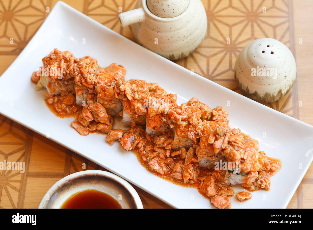 Blick von oben auf Fusion-Sushi-Brötchen, die großzügig mit herzhaftem Lachs belegt sind, serviert auf einem weißen Teller für eine kühne, moderne Note der japanischen Küche. Stockfoto
