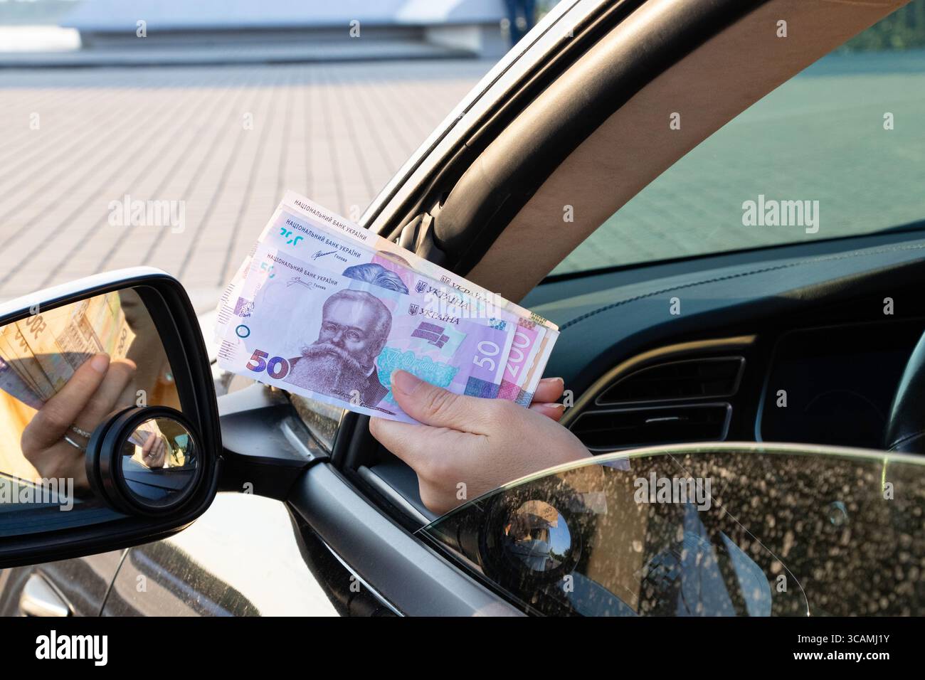 Die Hand einer Frau hält Griwna-Rechnungen von einem Autogeld in einem Auto als Bestechung oder Zahlung, bar in der Hand Stockfoto