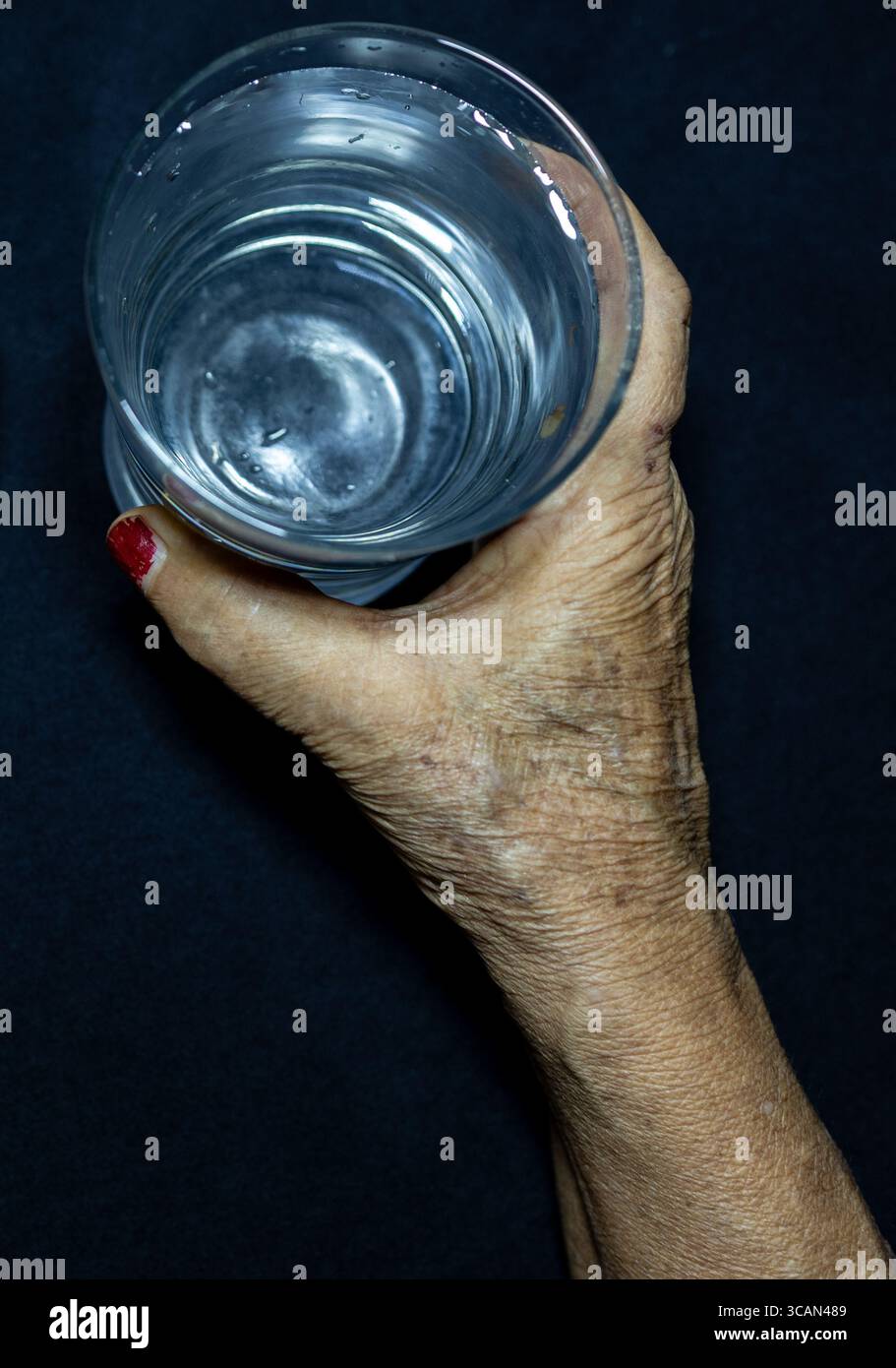 Ältere Hand mit einem Glas frisches Trinkwasser im Innenlicht Stockfoto