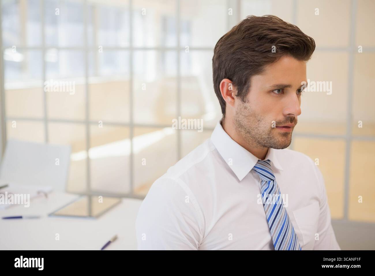 Männlicher Mitarbeiter, der Dokumente am Schreibtisch überprüft, trägt Krawatte in der Nähe einer Brille mit Monitor-Stift, Kopierraum Stockfoto
