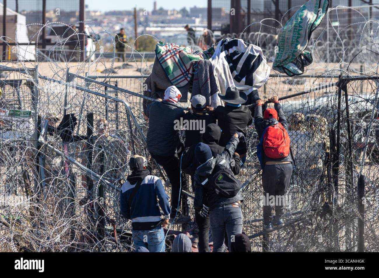 Zivilisten, die Habseligkeiten tragen, navigieren in einem verzweifelten Migrationsversuch durch einen Stachelzaun in Ciudad Ju?rez. Stockfoto