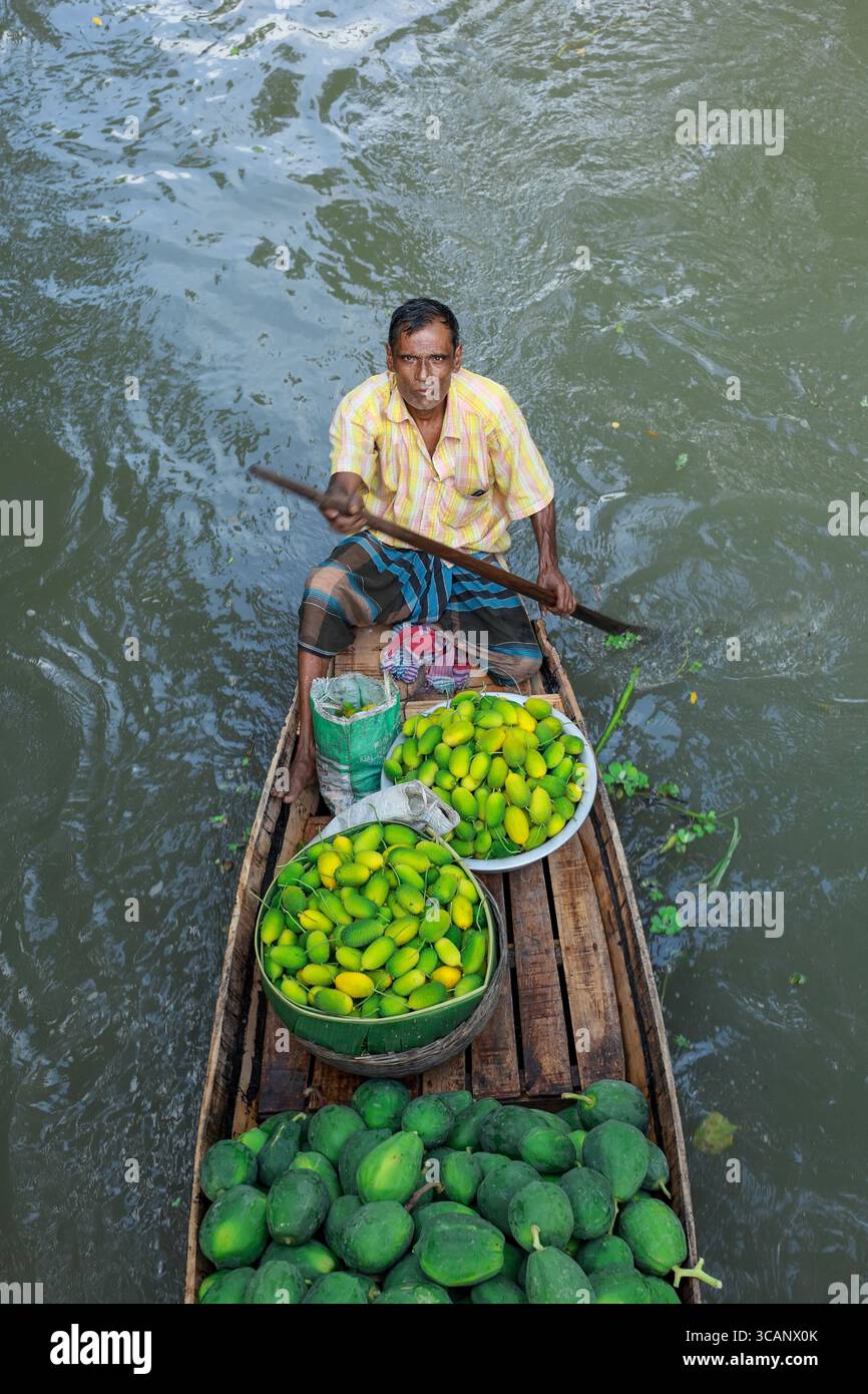 Barishal, Bangladesch - 9. August 2018: Blick auf einen Mann, der ein Boot mit lebhaftem grünem Gemüse entlang einer Wasserstraße rudert und das Tageslicht reflektiert Stockfoto Barishal, Bangladesch - 9. August 2018: Blick auf einen Mann, der ein Boot mit lebhaftem grünem Gemüse entlang einer Wasserstraße rudert und das Tageslicht reflektiert Stockfoto