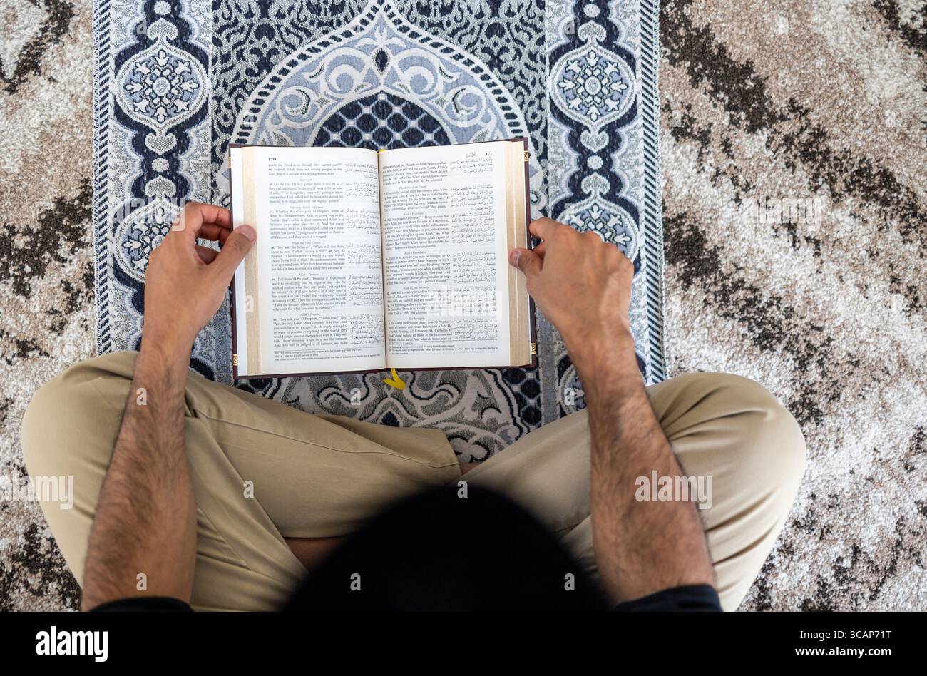 Muslimischer Mann liest den Koran, während er auf einer Gebetsmatte sitzt Stockfoto