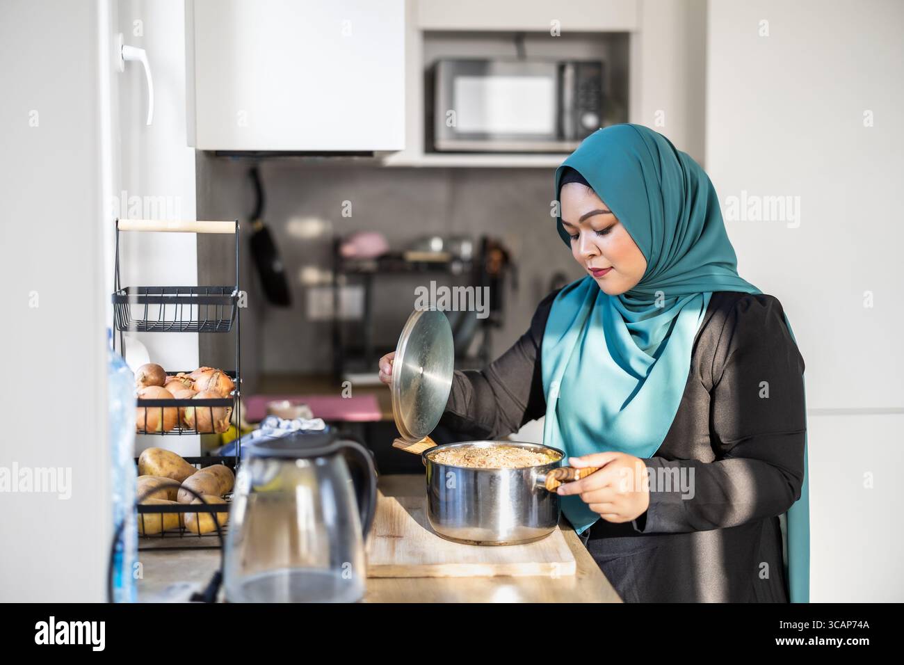 Muslimische Frau, die in der modernen Küche steht und Hijab trägt Stockfoto