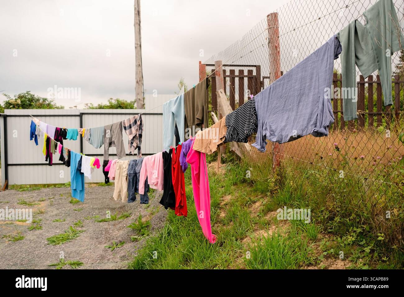 Bunte Kleidung hängt an einem Seil, das an einem Holzzaun befestigt ist, und trocknet im Sonnenlicht. Einfaches Alltagskonzept mit natürlichen Texturen. Stockfoto