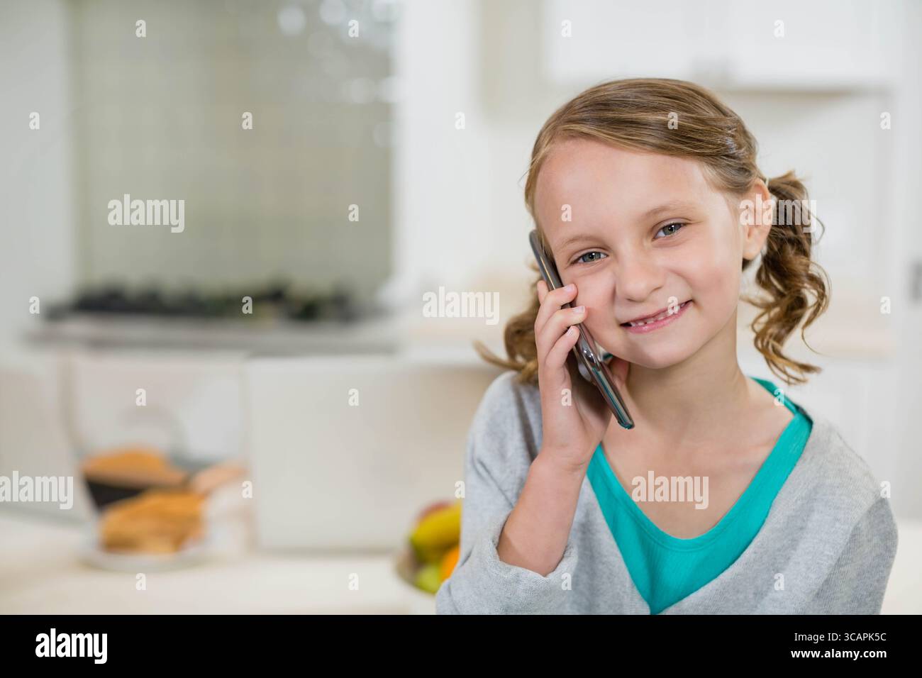 Mädchen, das das Smartphone am Ohr hält, steht in der Küche in der Nähe von Obstschale und Brot, Kopierraum Stockfoto
